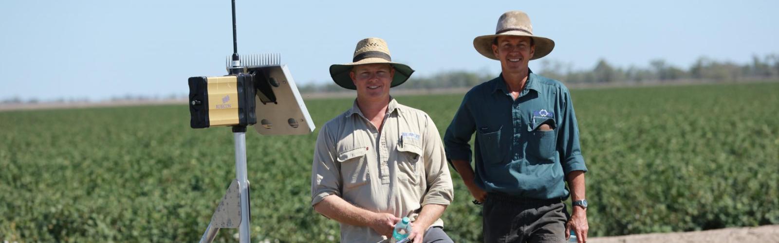 Two cotton growers standing in a cotton field with irrigation technology. 